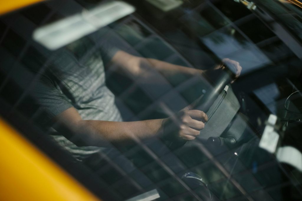 Durch die Windschutzscheibe eines männlichen Fahrers ethnischer Herkunft im Taxi während der Arbeit in der Stadt
