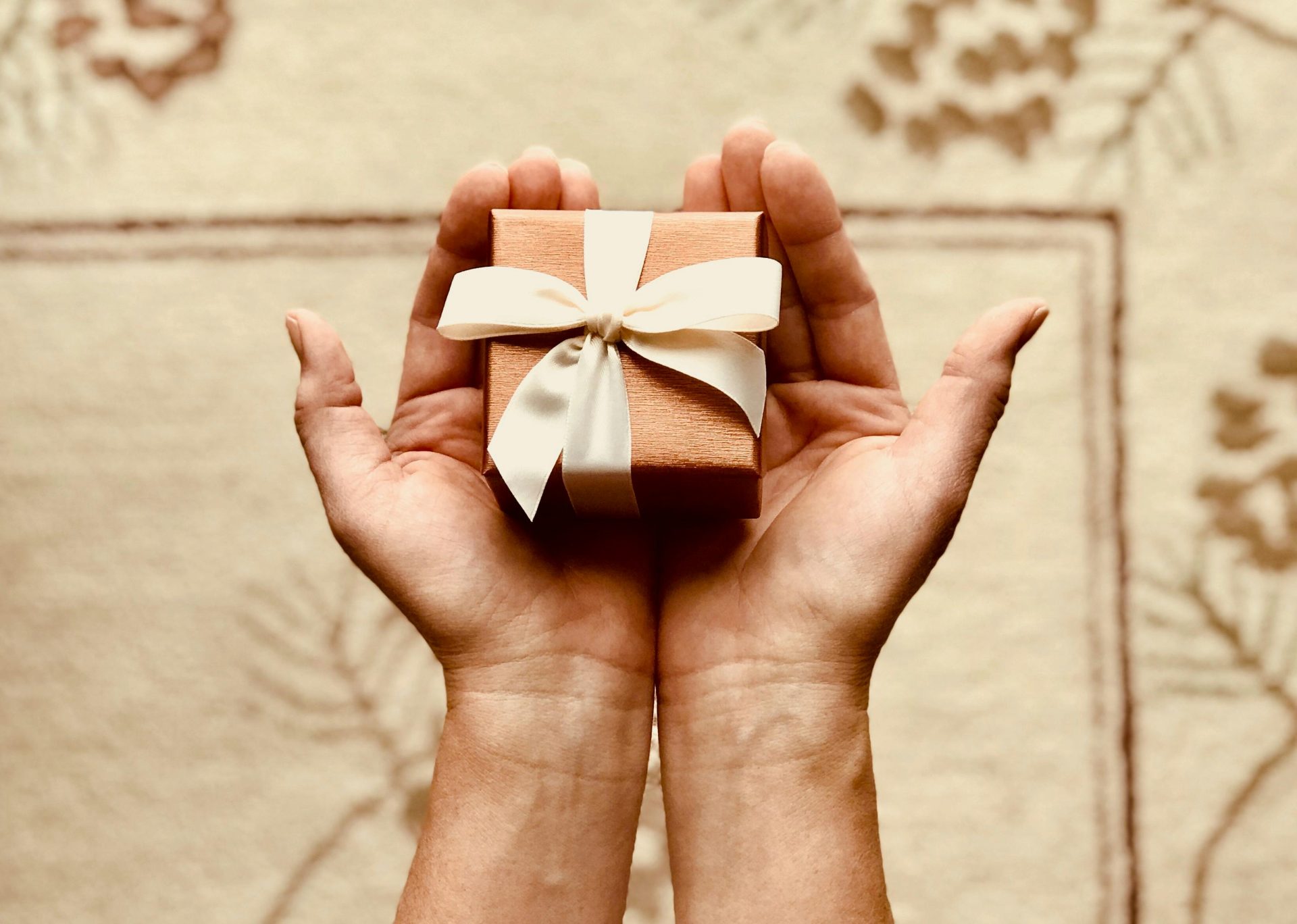 Nahaufnahme von Händen, die eine wunderschön verpackte Geschenkbox mit einer Schleife halten, perfekt für Feiern und Überraschungen.